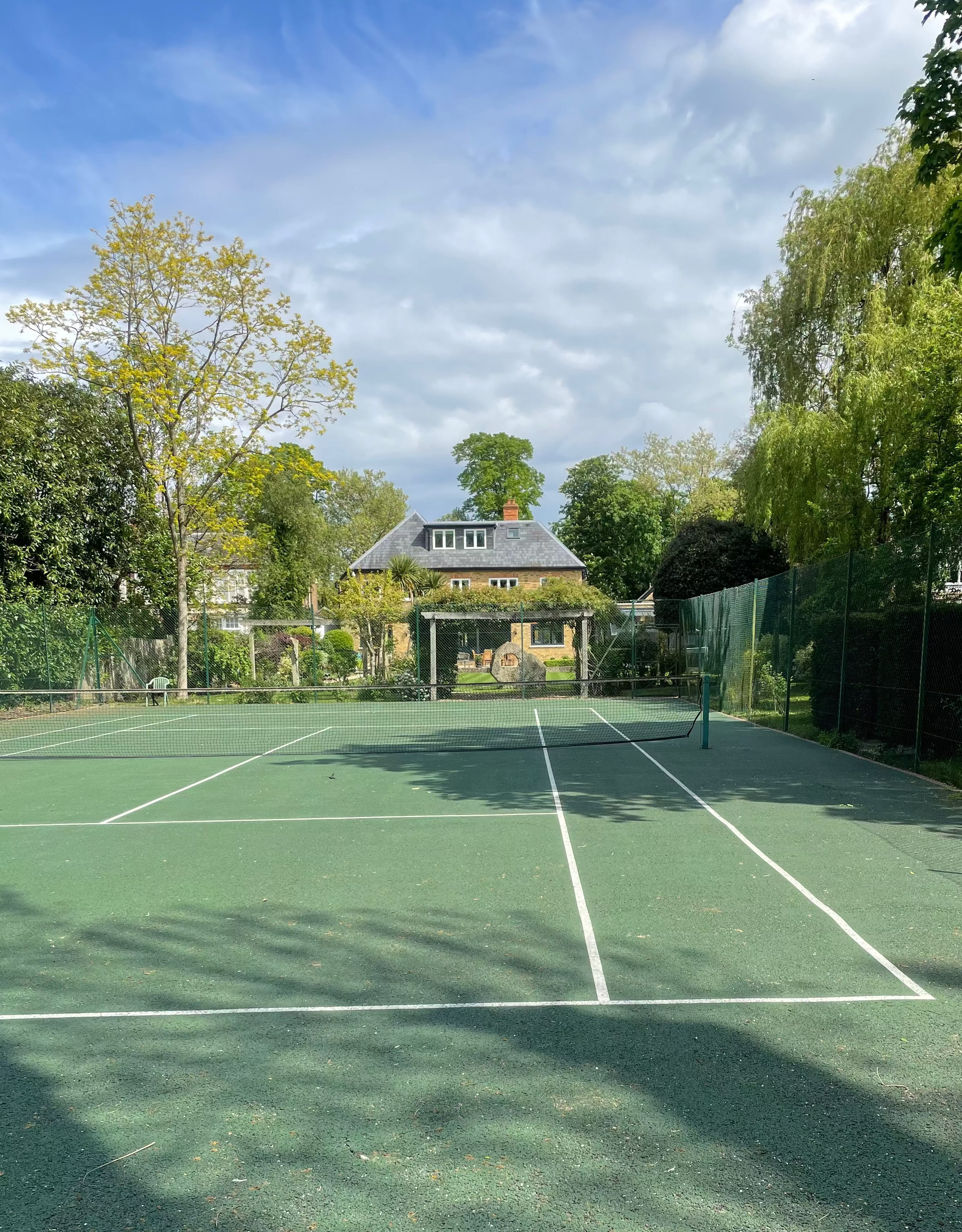 Tennis court with trees and a house in the background