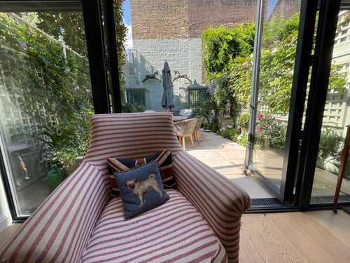 Striped armchair with a cushion featuring a dog design, set against a backdrop of a garden and building.