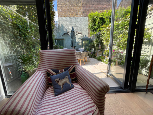 Striped armchair with a cushion featuring a dog design, set against a backdrop of a garden and building.