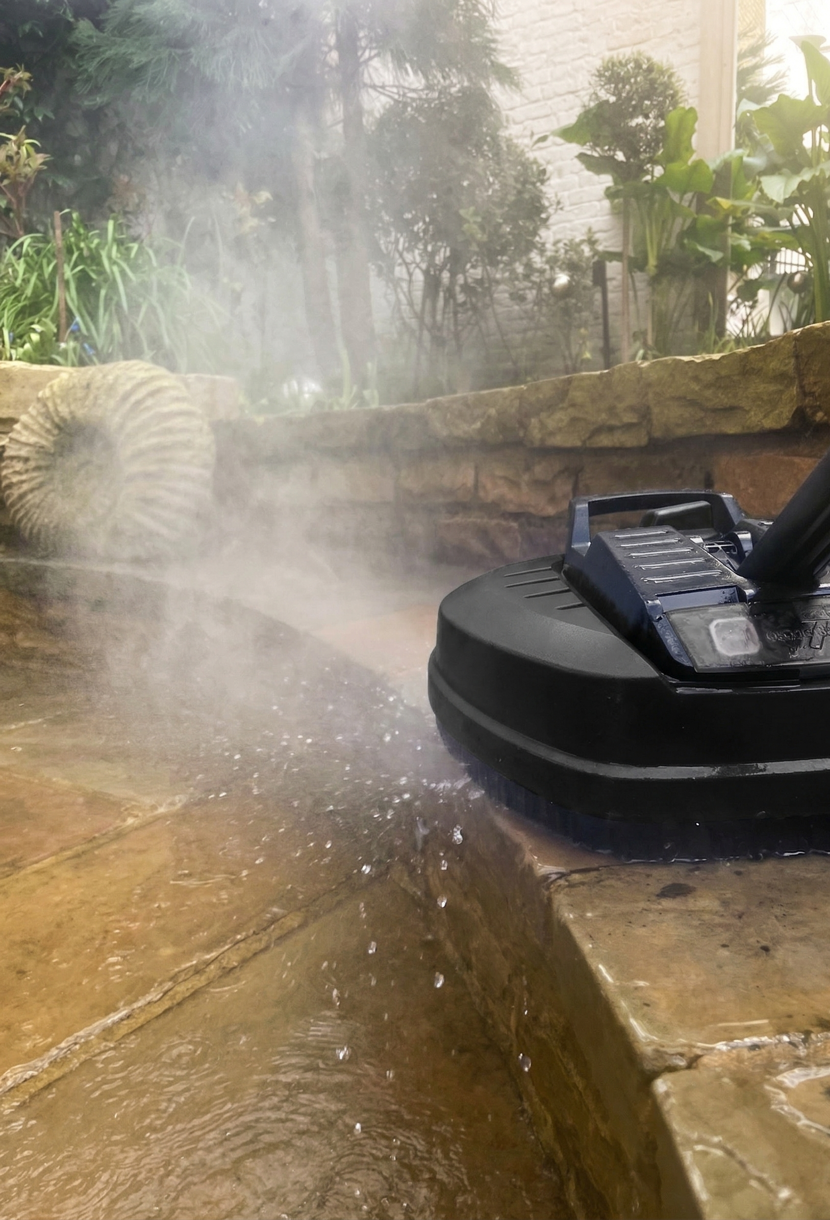 Professional jet washing for a natural stone patio in London. Holmes Gardens uses specialized surface cleaners to ensure deep cleaning without damaging the masonry or surrounding botanical features.