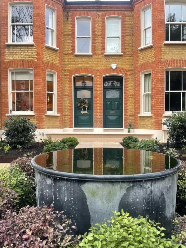 Brick house with two green doors and a reflecting pool in front